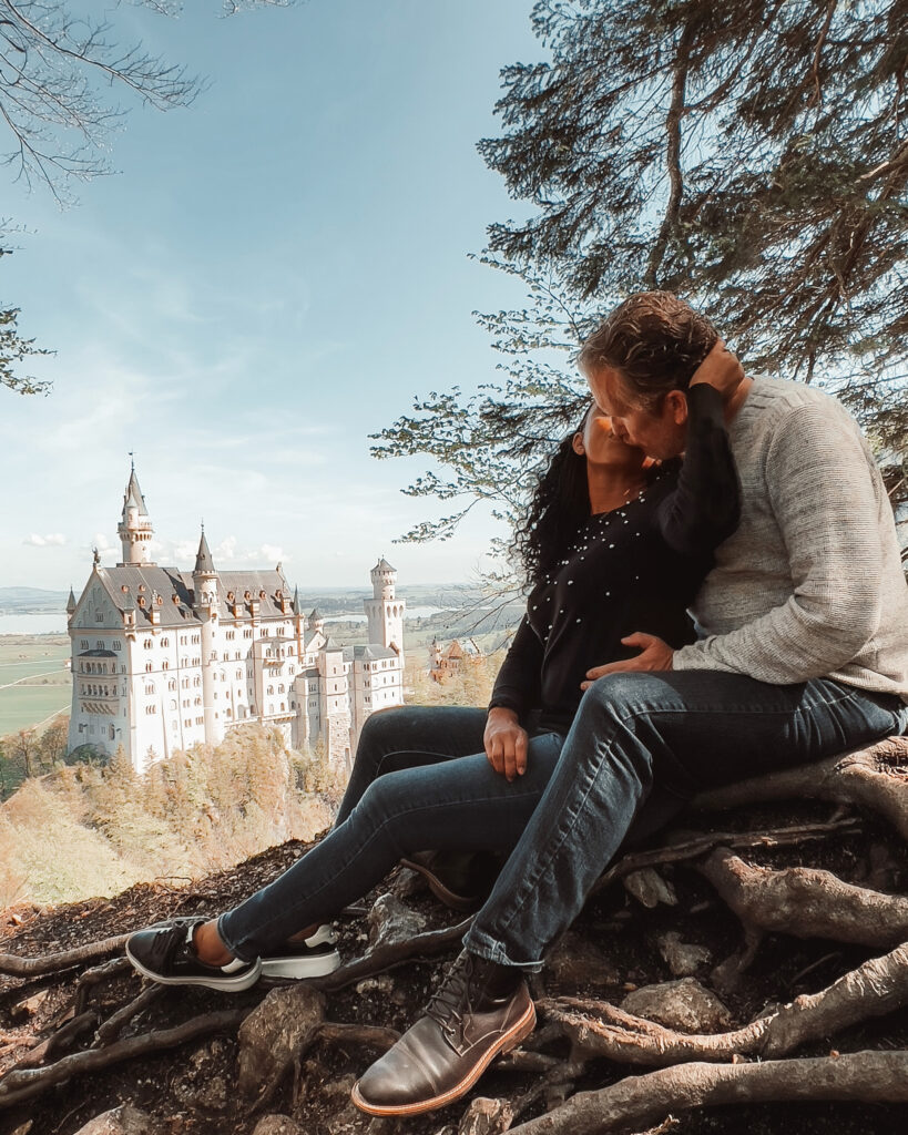 Couple kisses while sitting on a hilltop overlooking Neuschwanstein Castle in Germany