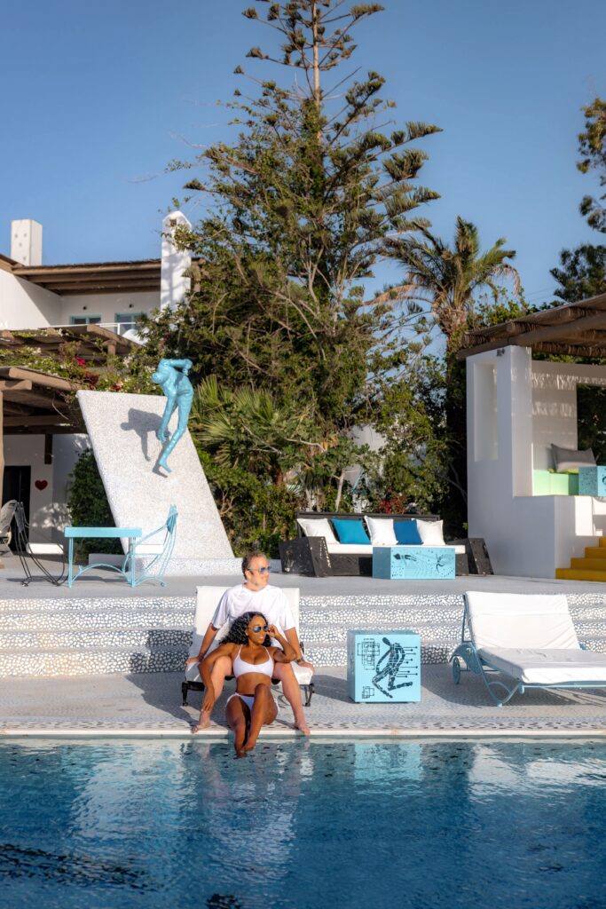 Couple sits on the edge of a sea front pool at the Agalia Resort in Ios, Greece