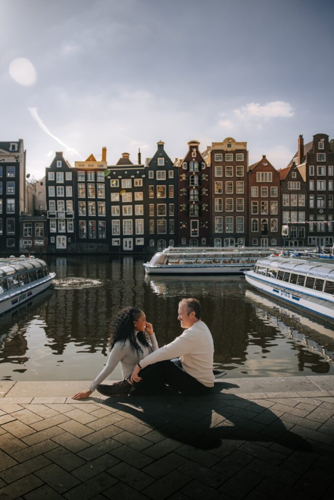 Couple chats and sits along the river in Damrak in Amsterdam