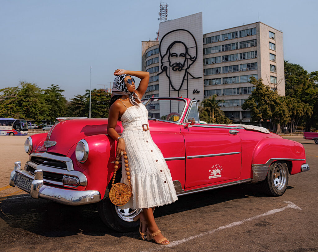 Woman leans against a vintage red convertible car in Revolutionary Square in Cuba