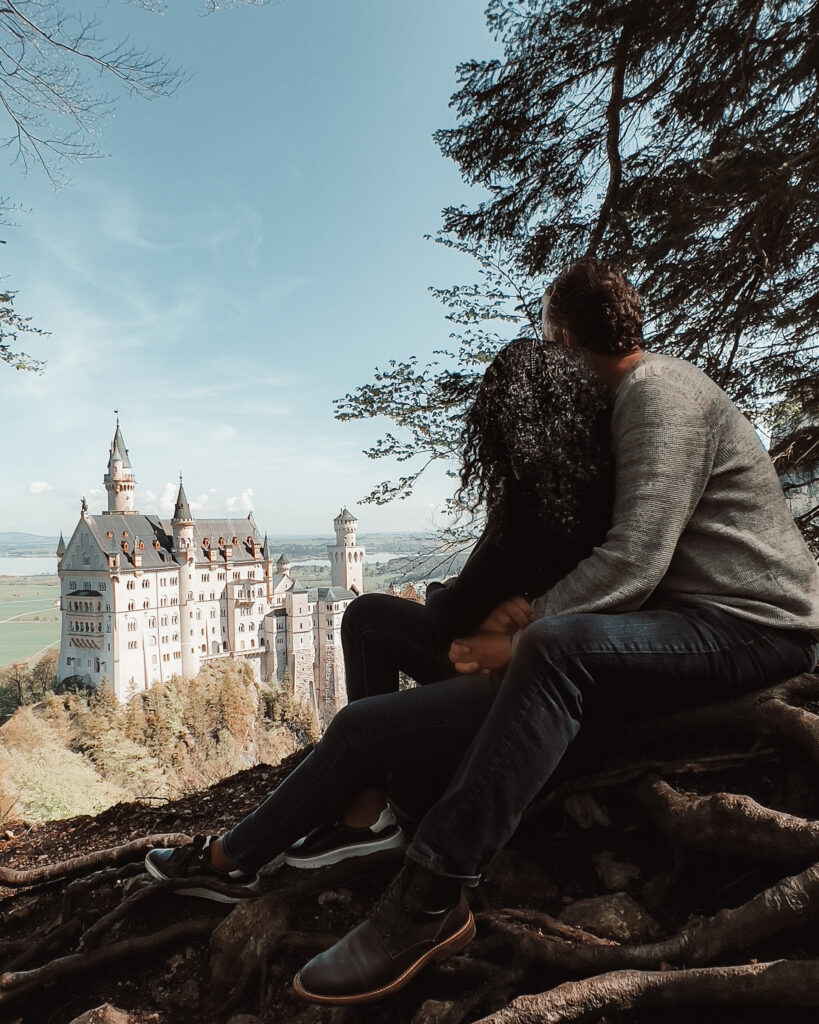 Couple embraces while sitting on a hilltop overlooking Neuschwanstein Castle in Germany