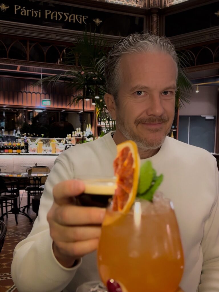 Brett Schneider raising a glass in a celebratory toast at Párisi Udvar Hotel Budapest as the holiday cheer lingers.